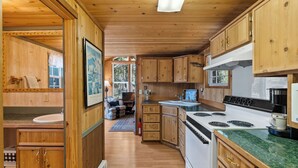 A wooden cabin interior with a kitchen featuring wooden cabinets, a stove, and a sink. - Gods County Cottage on Swan River (Bigfork)