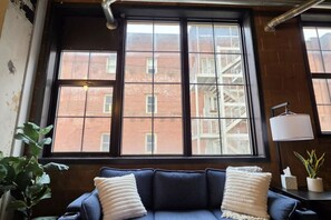 A room with a large window, a blue sofa, and a potted plant.