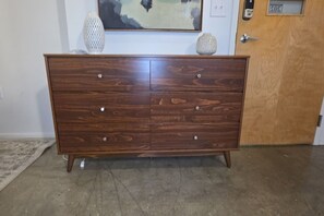 A wooden dresser with two drawers and four knobs, placed in a room with a concrete floor and a door in the background.