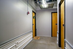 En smal hall med två trädörrar, en lampa och en dörrmatta på golvet.