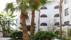 A courtyard with palm trees, a water feature, and a white building with arched windows. - Perla Blanca by Interhome (Peñiscola)