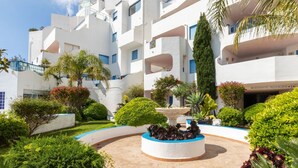 A modern building with a courtyard featuring a central fountain, surrounded by well-maintained greenery and a clear blue sky. - Perla Blanca by Interhome (Peñiscola)