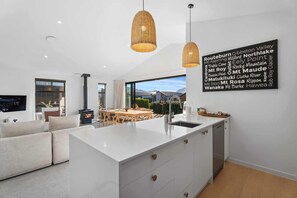 Een moderne keuken met een centraal eiland, hangende verlichting en uitzicht op de omgeving.