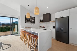 A modern kitchen with a large island, bar stools, a black refrigerator, and a view of mountains.