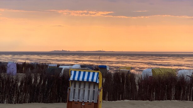 Escena de playa con una silla de playa a rayas, una valla y una costa distante.