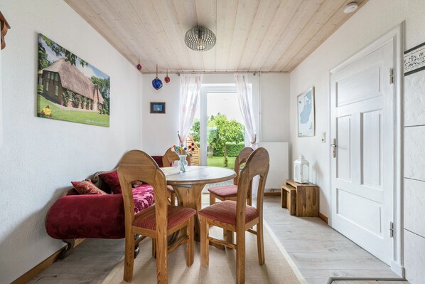 A dining area with a wooden table and chairs, a red sofa, and a painting of a house on the wall.