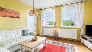 Ein Wohnzimmer mit einer Couch, einem Holztisch, einem roten Teppich, einem Fernseher und einem Fenster mit Vorhängen.
