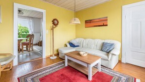 Ein Zimmer mit einem weißen Sofa, einem Holztisch, einem roten Teppich, Holzdielen, einem Deckenventilator und einem Bild an der Wand.