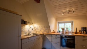 Eine Küche mit weißen Schränken, einem Backofen, einer Spüle und einem Fenster mit Tageslicht.