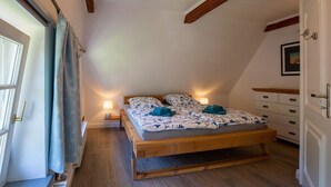 Ein Schlafzimmer mit einem hölzernen Bett, einem Nachttisch mit Lampe, einem Fenster mit Vorhängen und einem Holzbalken an der Decke.