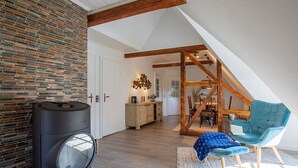 Ein Loft-Zimmer mit freiliegenden Holzbalken, einer Steinwand, einem schwarzen Heizkörper, einem blauen Stuhl und einer Treppe, die zu einer Erkerzone führt.