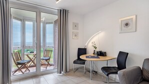 A room with a sliding glass door leading to a balcony, a round table with chairs, and a sofa. - Studio 'With Great Sea View of Island' with Sea View, Private Garden and Wi-Fi (Cuxhaven)