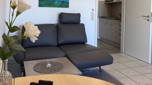A modern living room with a sofa, a painting, a vase with flowers, and a table with binoculars. - Studio 'With Great Sea View of Island' with Sea View, Private Garden and Wi-Fi (Cuxhaven)