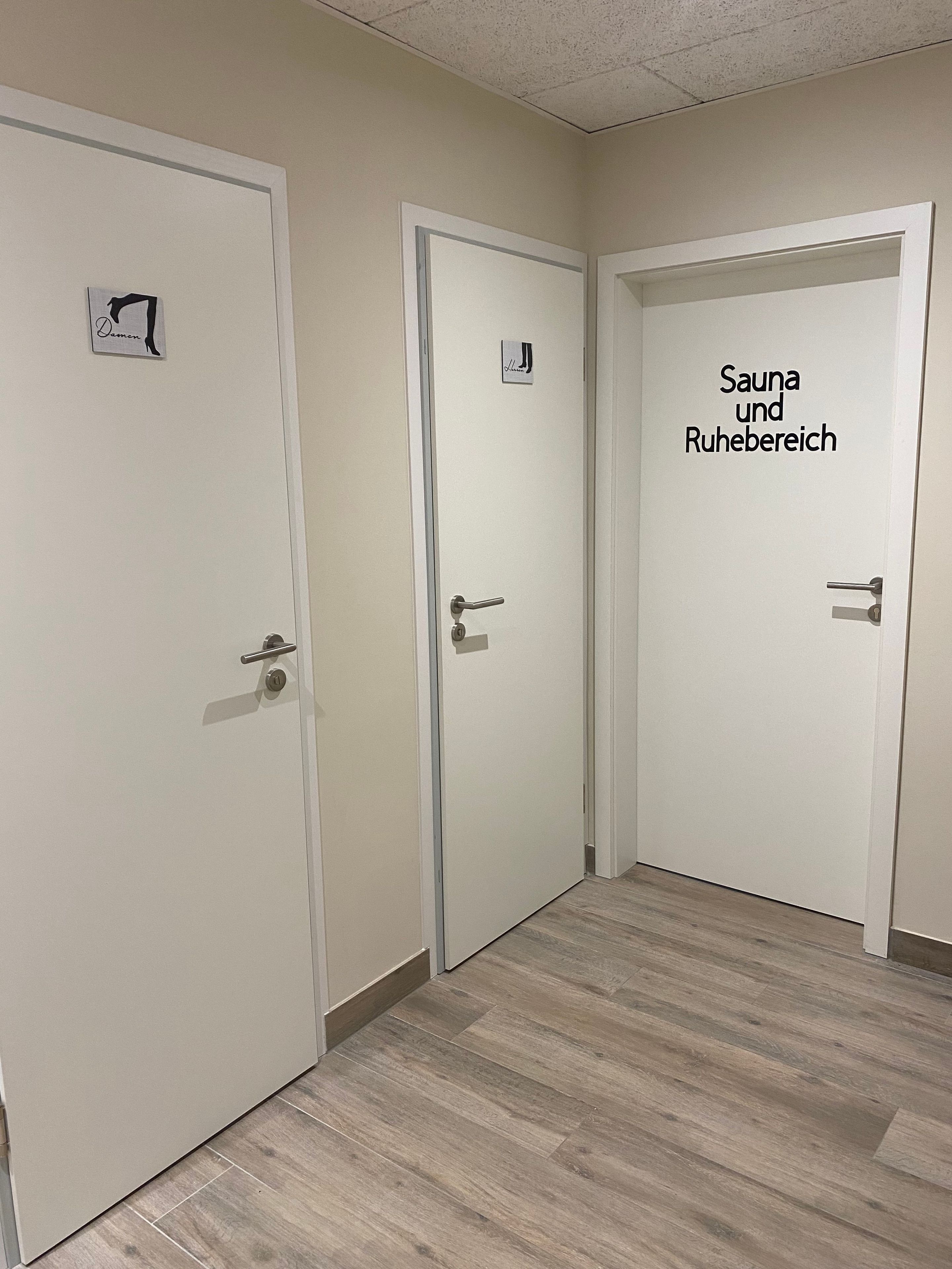 Drei weiße Türen, wobei an der rechten Tür ein Schild auf eine Sauna und einen Entspannungsbereich hinweist.