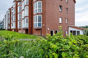 A multi-story residential building with a brick facade, large windows, and a small garden area in the foreground.