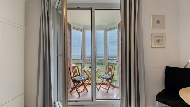 A room with a sliding glass door leading to an outdoor patio with two chairs and a table. - Studio 'With Great Sea View of Island' with Sea View, Private Garden and Wi-Fi (Cuxhaven)