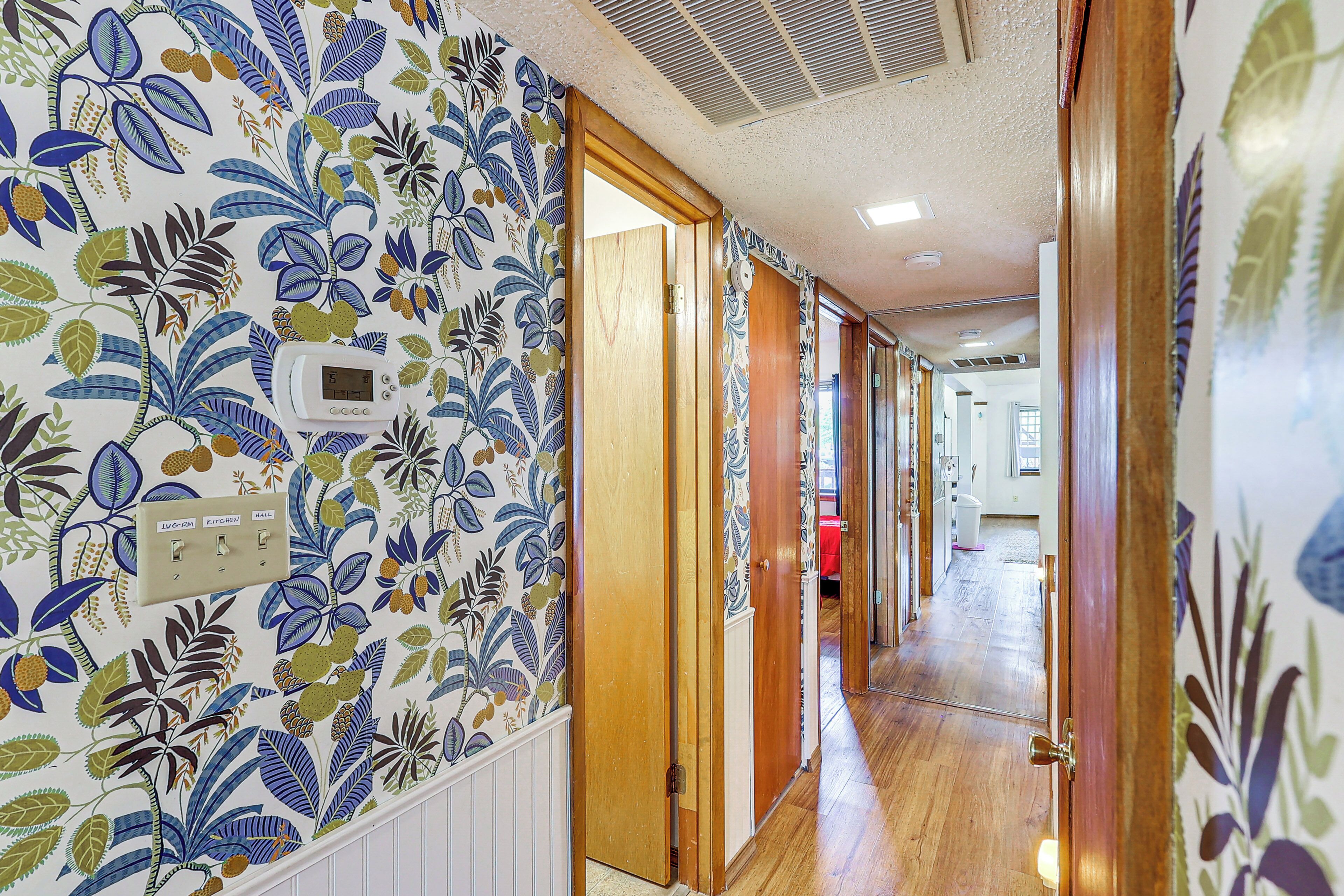 Un couloir avec un papier peint à motifs, des portes en bois et un thermostat fixé au mur.