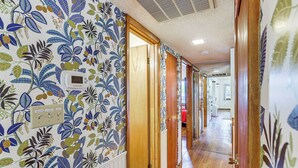 Un couloir avec un papier peint à motifs, des portes en bois et un thermostat fixé au mur.