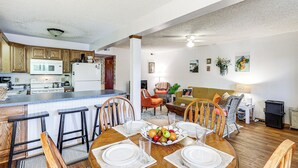 Une cuisine moderne avec des meubles en bois, un îlot central doté de tabourets de bar et un coin repas avec une table en bois, dressée pour quatre personnes.