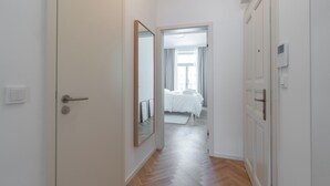 A hallway leading to a bedroom with a bed, a mirror, and a door with a light switch. - Apartment in Clouds Letná Luxury Balcony (Prague)