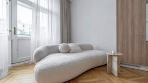 A modern, minimalist room with a curved sofa, a small side table, and a wooden wardrobe. - Apartment in Clouds Letná Luxury Balcony (Prague)