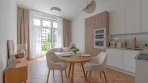 A modern kitchen with a dining area, featuring a round wooden table, white chairs, and a vase with flowers. - Apartment in Clouds Letná Luxury Balcony (Prague)