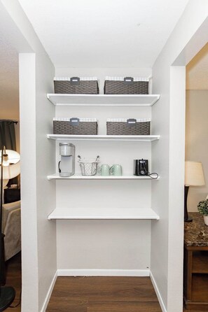 A white wall with three shelves, each holding baskets and a coffee maker. - One Bedroom Hideaway near NDSU (Fargo)