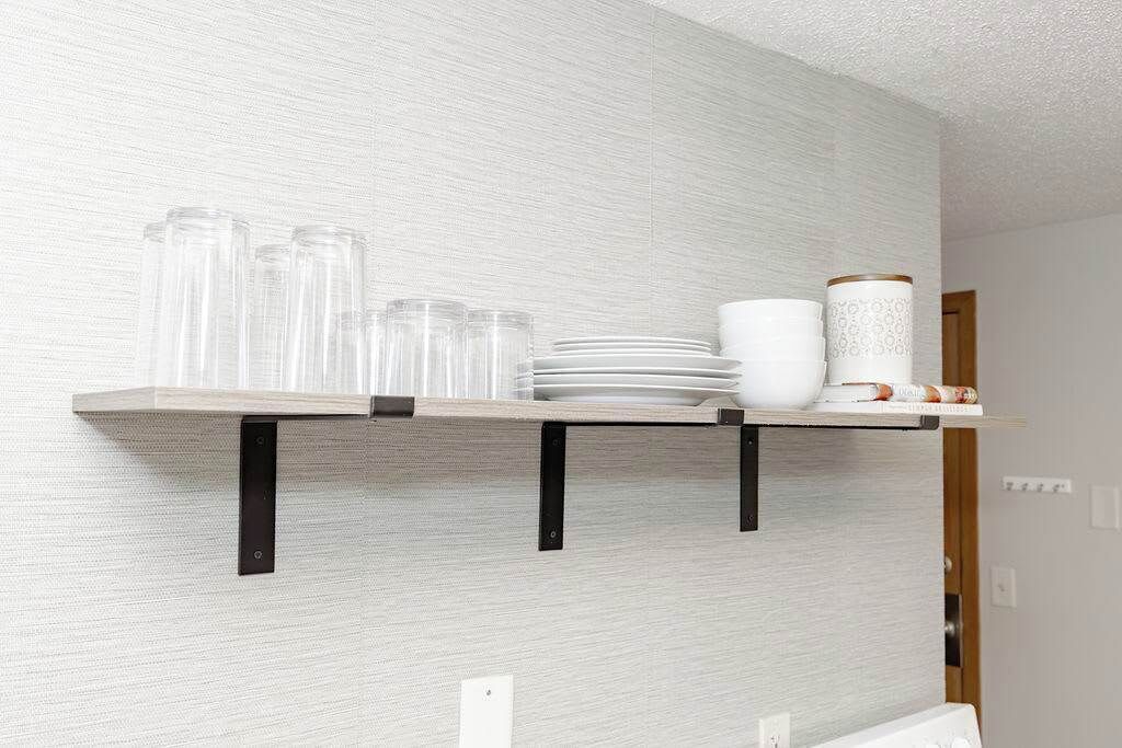 A kitchen shelf with clear glassware, white plates, and a decorative vase.