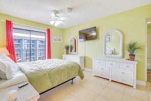 Een slaapkamer met een bed, een dressoir, een televisie en een balkon met rode gordijnen.