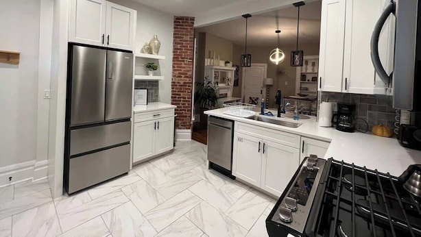 Una cocina moderna con armarios blancos, un refrigerador de acero inoxidable, lavavajillas integrado, estufa a gas e iluminación colgante.