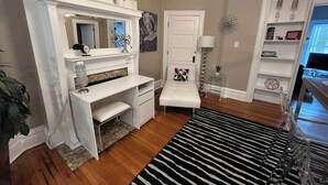 Una habitación con escritorio blanco, banca, chimenea y estantería.