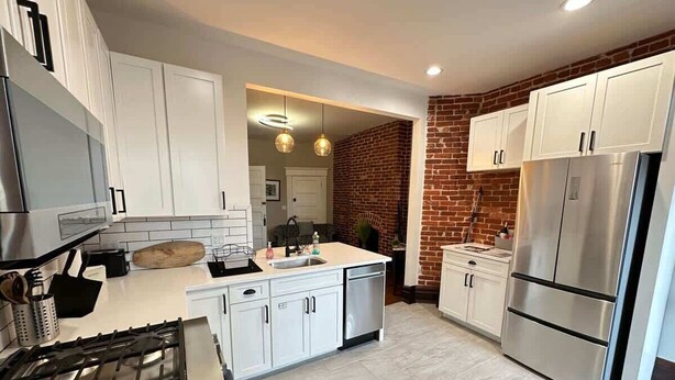 A modern kitchen with white cabinets, a stainless steel refrigerator, and a brick accent wall.