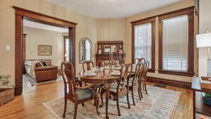 A dining room with a wooden table set for six, surrounded by matching chairs. There is a large mirror above the table and a window with blinds to the right. - 4 Bed 2 Bath Townhouse - Goodale Park (Columbus)