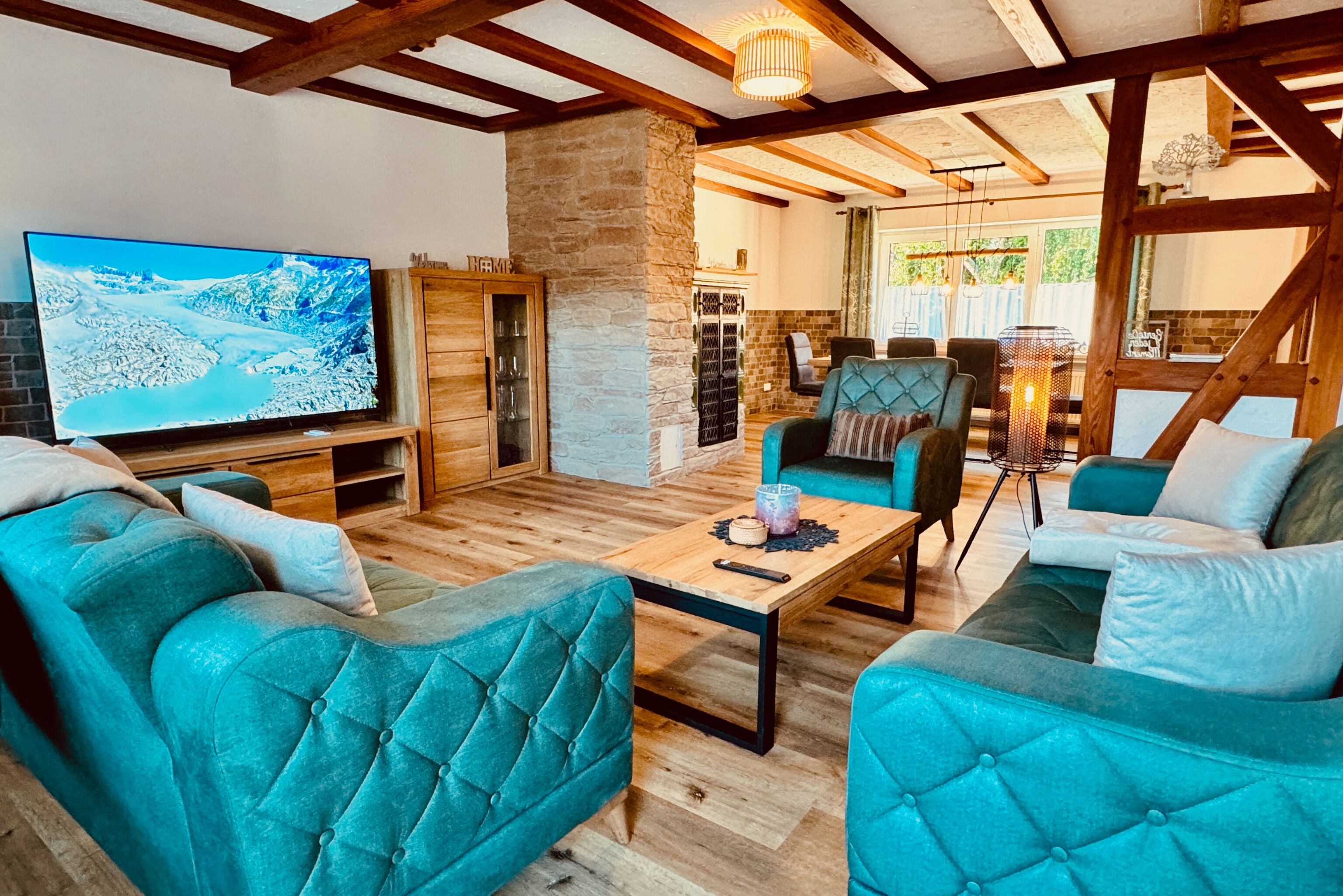 Ein gemütliches Wohnzimmer mit senffarbenen Polstersofas, einem Holztisch und einem großen Flachbildfernseher, der eine verschneite Landschaft zeigt.