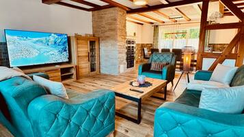 Ein gemütliches Wohnzimmer mit senffarbenen Polstersofas, einem Holztisch und einem großen Flachbildfernseher, der eine verschneite Landschaft zeigt.