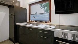 Una cocina moderna con armarios oscuros, un lavamanos de acero inoxidable, una ventana con persianas y un horno empotrado.