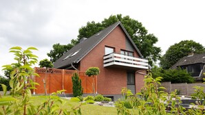 Una casa moderna con techo inclinado, balcón y patio cercado.