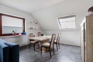 Un coin repas avec une table et des chaises en bois, une fenêtre et un radiateur.