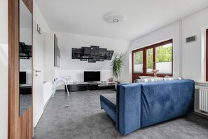 Un salon moderne avec un canapé, un téléviseur, une plante et une œuvre d’art représentant un paysage urbain accrochée au mur.