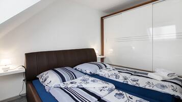 A bedroom with a bed, a nightstand, a wall-mounted shelf, and a wardrobe.