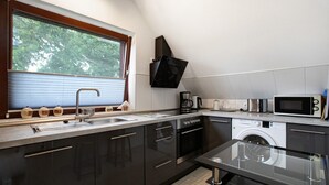 Una cocina moderna con lavavajillas, microondas y horno integrados, una ventana con persianas y un fregadero.
