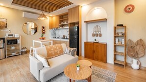 A modern living room with a sofa, coffee table, and a kitchen area with wooden cabinets and a refrigerator. - 2BR Private Pool Villa Dove By Orivista (Mengwi)