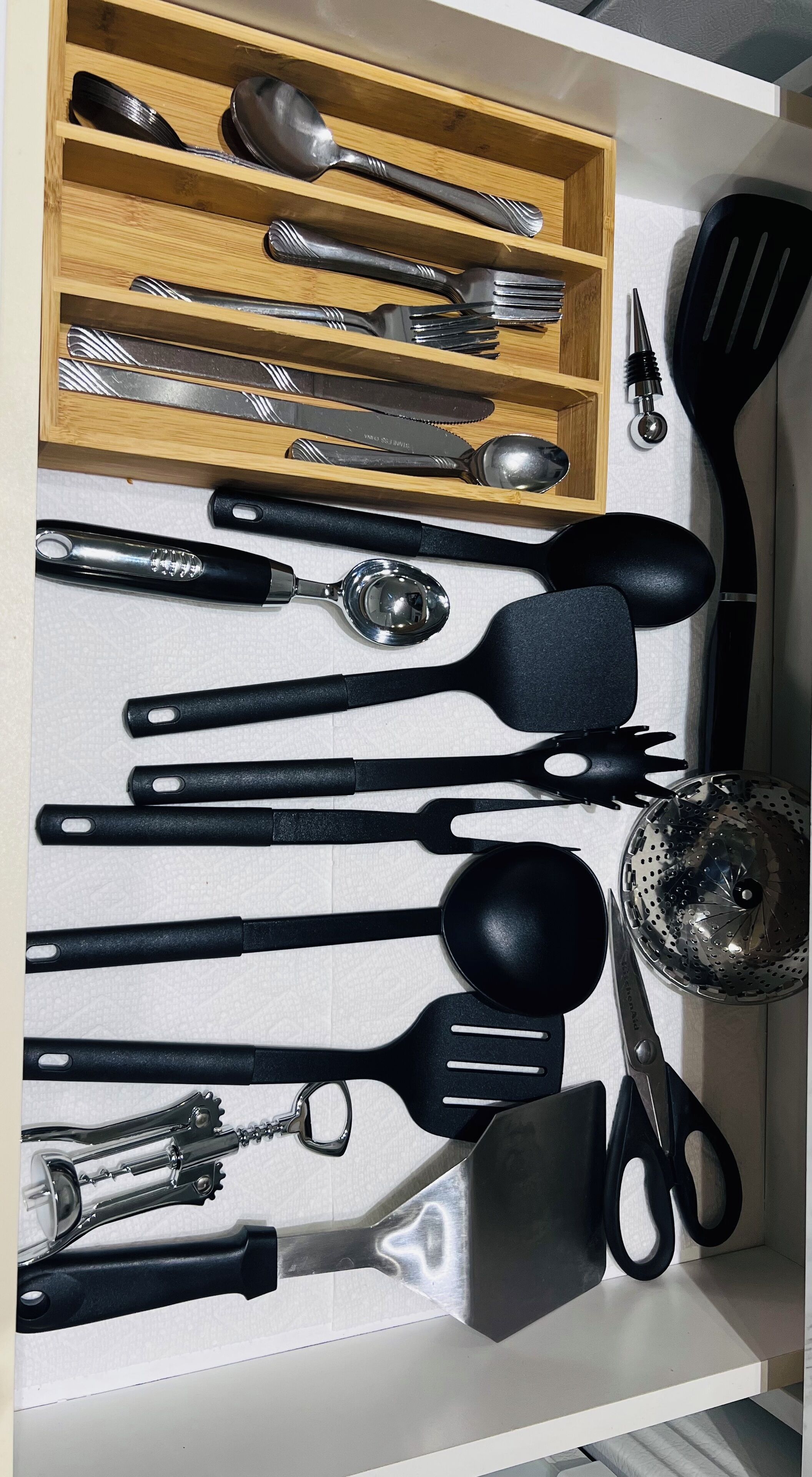 A drawer with various kitchen utensils including spoons, forks, knives, spatulas, and a colander.