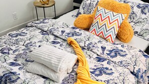 Een net opgemaakt bed met bloemenbeddels, een zachte oranje deken en een decoratief kussen.