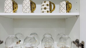 Een plank met vier witte mokken met gouden patronen en handgrepen, en vier glazen wijnglazen met gouden randen en de tekst 'BRALILLE' erop gegraveerd.