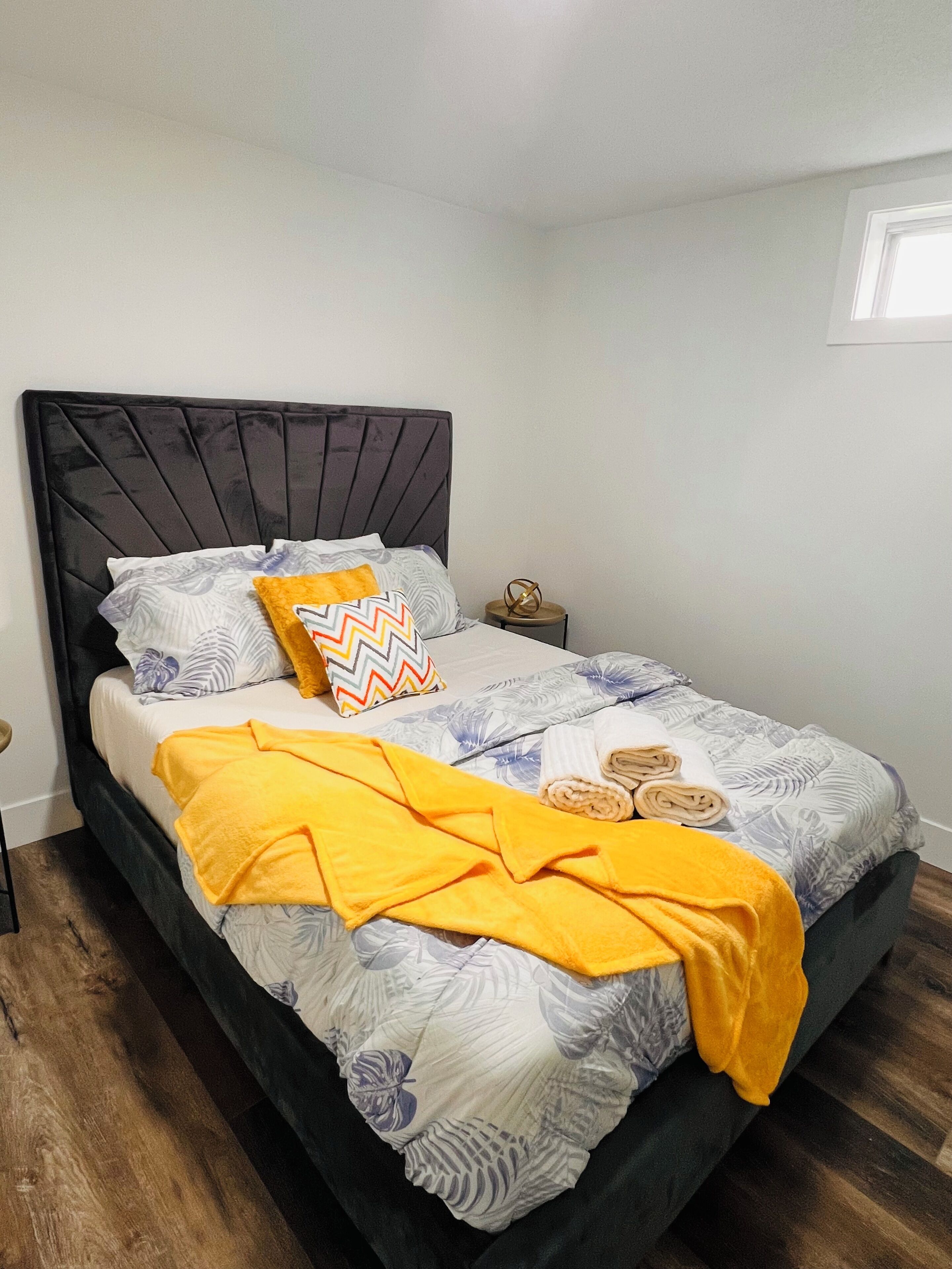 A neatly made bed with a patterned bedspread, a yellow throw blanket, and decorative pillows.