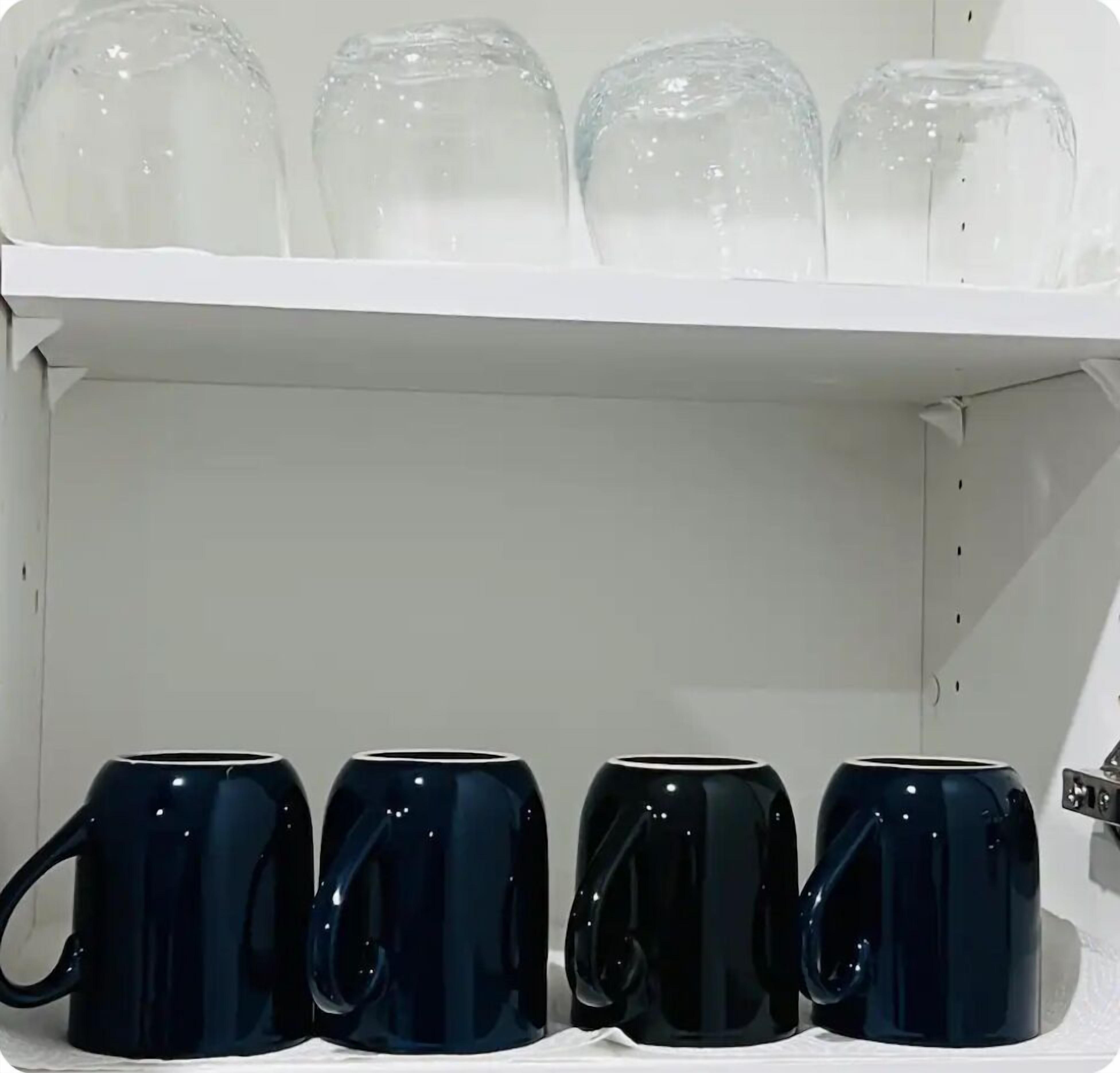 A shelf with four clear glass mugs and four dark blue ceramic mugs.