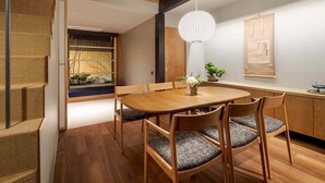 Un comedor con una mesa y sillas de madera, una lámpara colgante y vista a un jardín por la ventana.