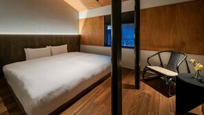 Un dormitorio moderno con una cama grande, vigas de madera en el techo, una ventana con persianas, una silla y una pequeña mesa con un florero.
