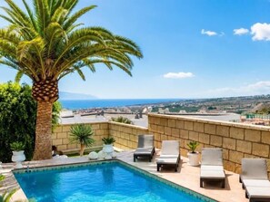 A rooftop pool with lounge chairs, a palm tree, and a view of the city. - Enchanting Villa Portocervo Heated Pool Sea view (Adeje)